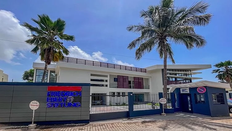 The building is the office of the Friedrich Ebert Foundation (FES) in Dakar, Senegal. It is a white, two-storey building with a modern entrance area, palm trees in the courtyard and a front wall bearing the foundation’s logo.