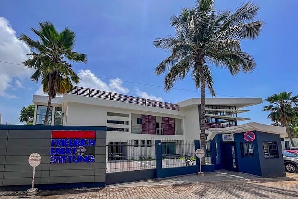 The building is the office of the Friedrich Ebert Foundation (FES) in Dakar, Senegal. It is a white, two-storey building with a modern entrance area, palm trees in the courtyard and a front wall bearing the foundation’s logo.